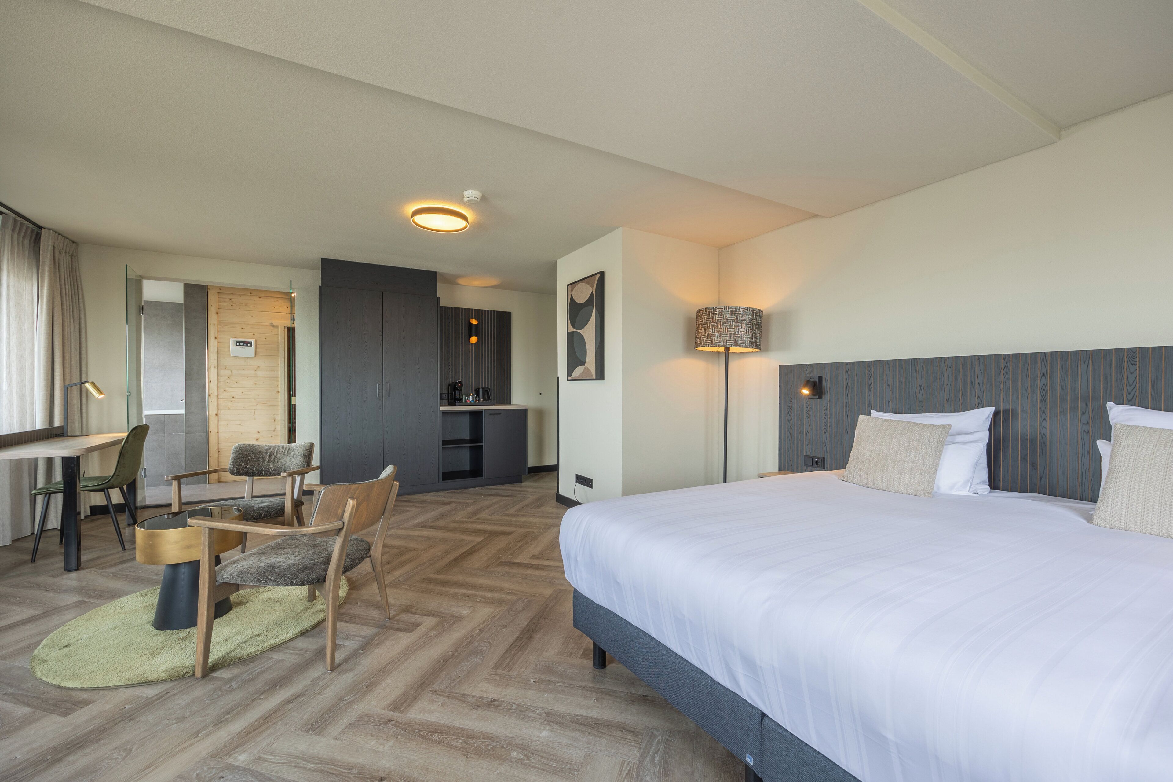 Ein Hotelzimmer mit einem großen Bett, einem Schreibtisch mit Stühlen, einer Küchenzeile und einem Badezimmer.