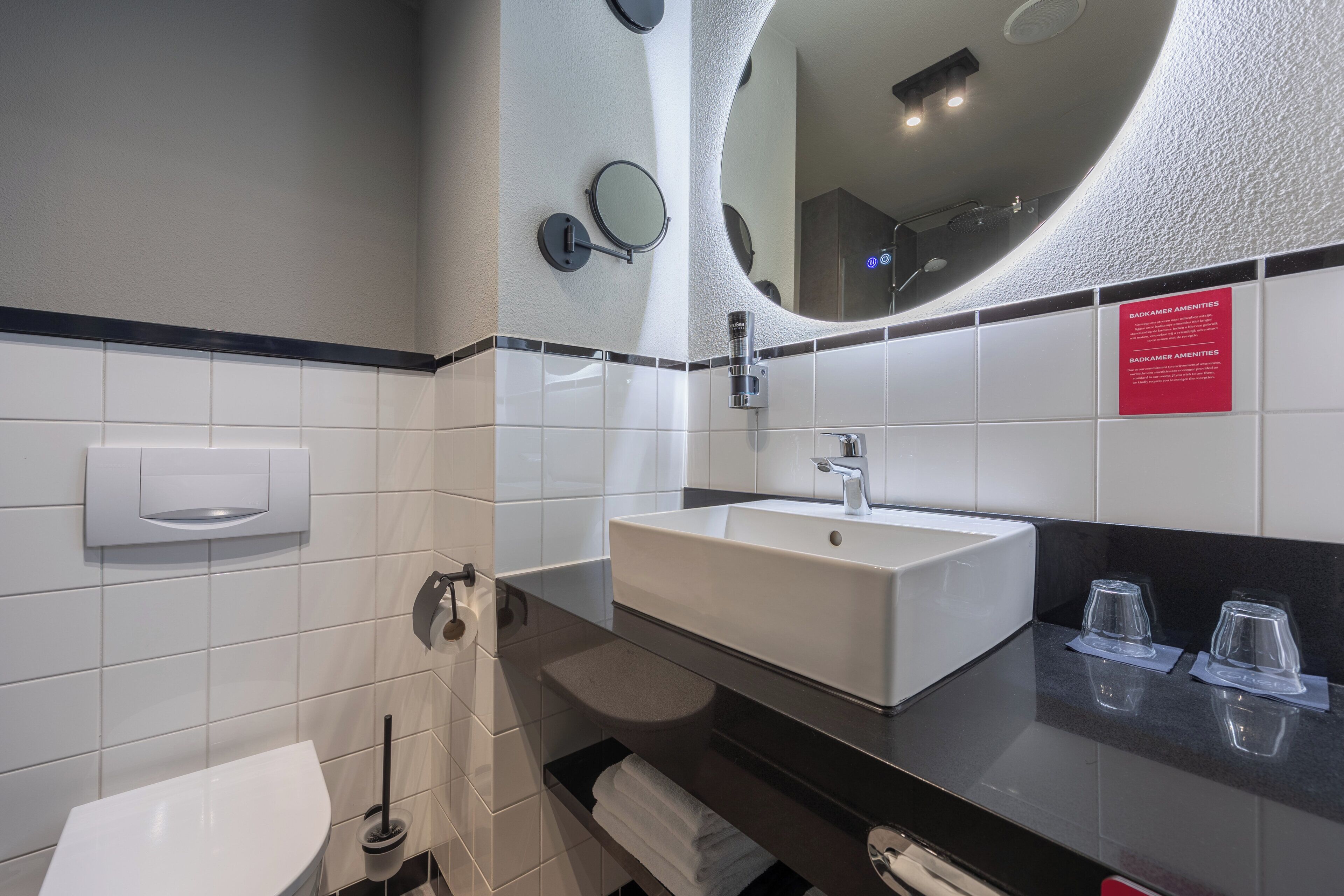 A modern bathroom with a white sink, mirror, and toilet. There are two glass tumblers on the counter.