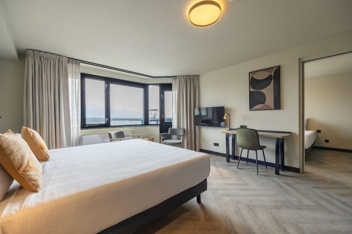 Une chambre d’hôtel avec un grand lit, un bureau, une chaise, une télévision et une vue sur l’extérieur.