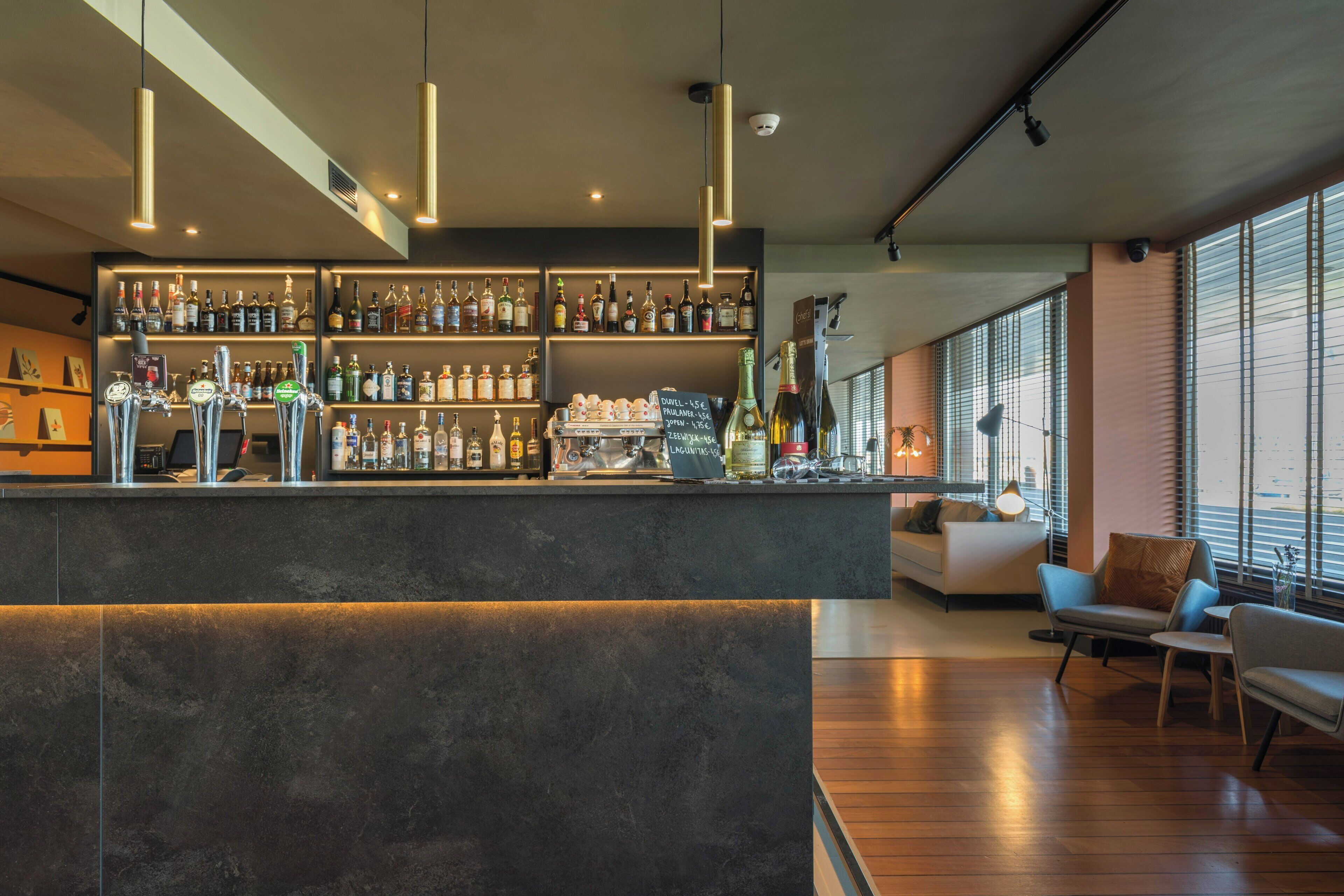 A modern bar area with a variety of liquor bottles, a coffee machine, and a seating area with a sofa and chairs.