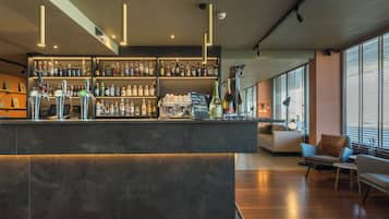 Een moderne bar met diverse drankflessen, een koffiemachine en een zithoek met een bank en stoelen.