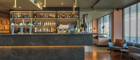 A modern bar area with a variety of liquor bottles, a coffee machine, and a seating area with a sofa and chairs.