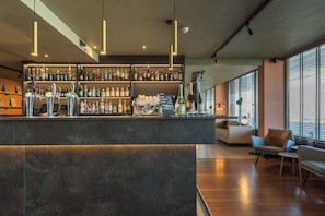Eine moderne Bar mit einer Auswahl an Spirituosen, einer Kaffeemaschine und einer Sitzecke mit Sofa und Sesseln.