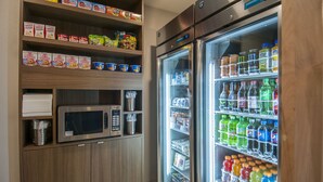A kitchenette with a microwave, shelves stocked with snacks, and a refrigerator filled with beverages. - Holiday Inn Express & Suites Plano West - Frisco by IHG (Plano)