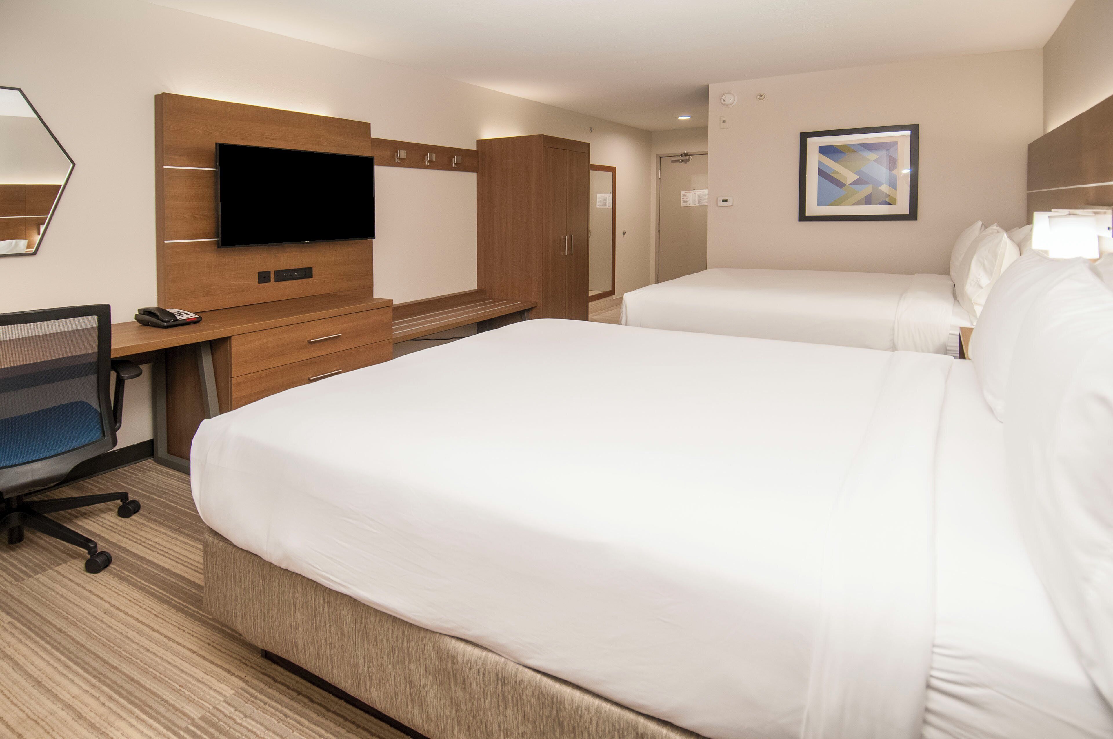 Une chambre d’hôtel avec deux lits, un bureau avec une chaise, un téléviseur à écran plat et un tableau au mur.