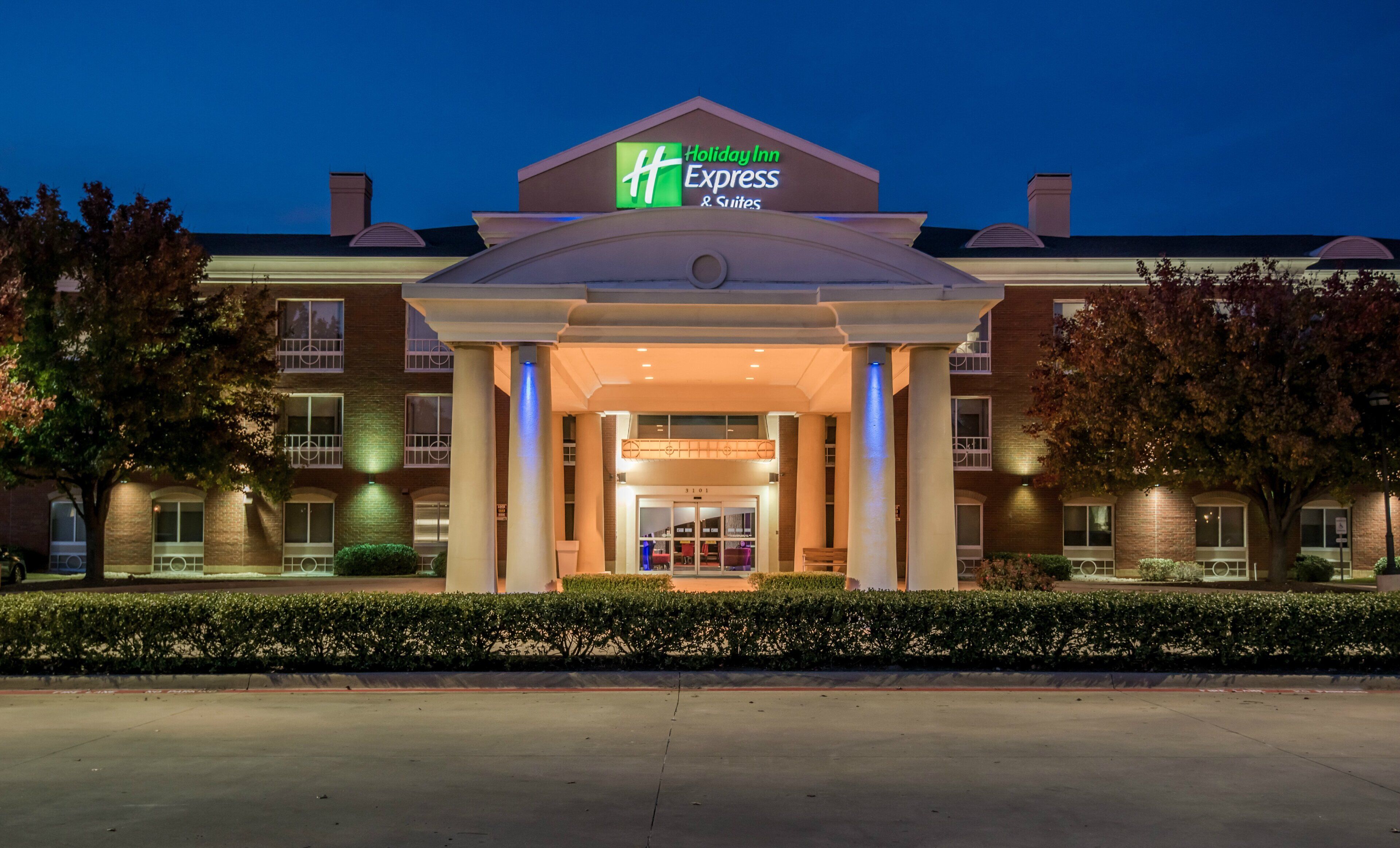 A Holiday Inn Express & Suites building with a prominent entrance, large columns, and a well-lit facade.
