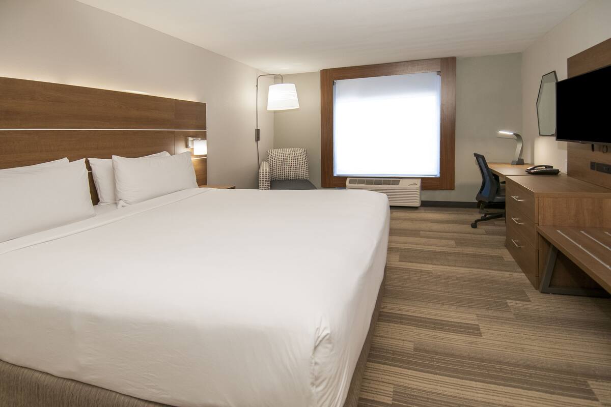 A hotel room with a large bed, a desk with a chair, a television, and a window.
