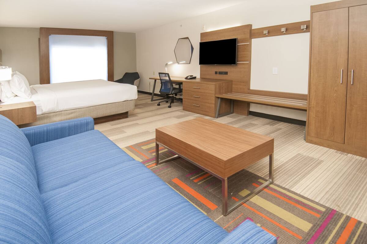 A hotel room with a bed, a desk with a chair, a television, and a wardrobe.