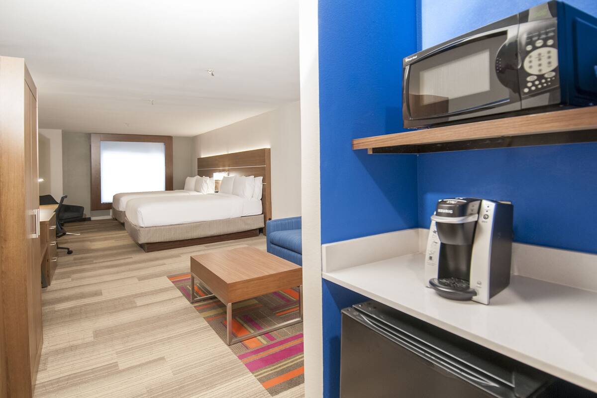 A hotel room with a bed, a desk, a microwave, and a coffee maker.