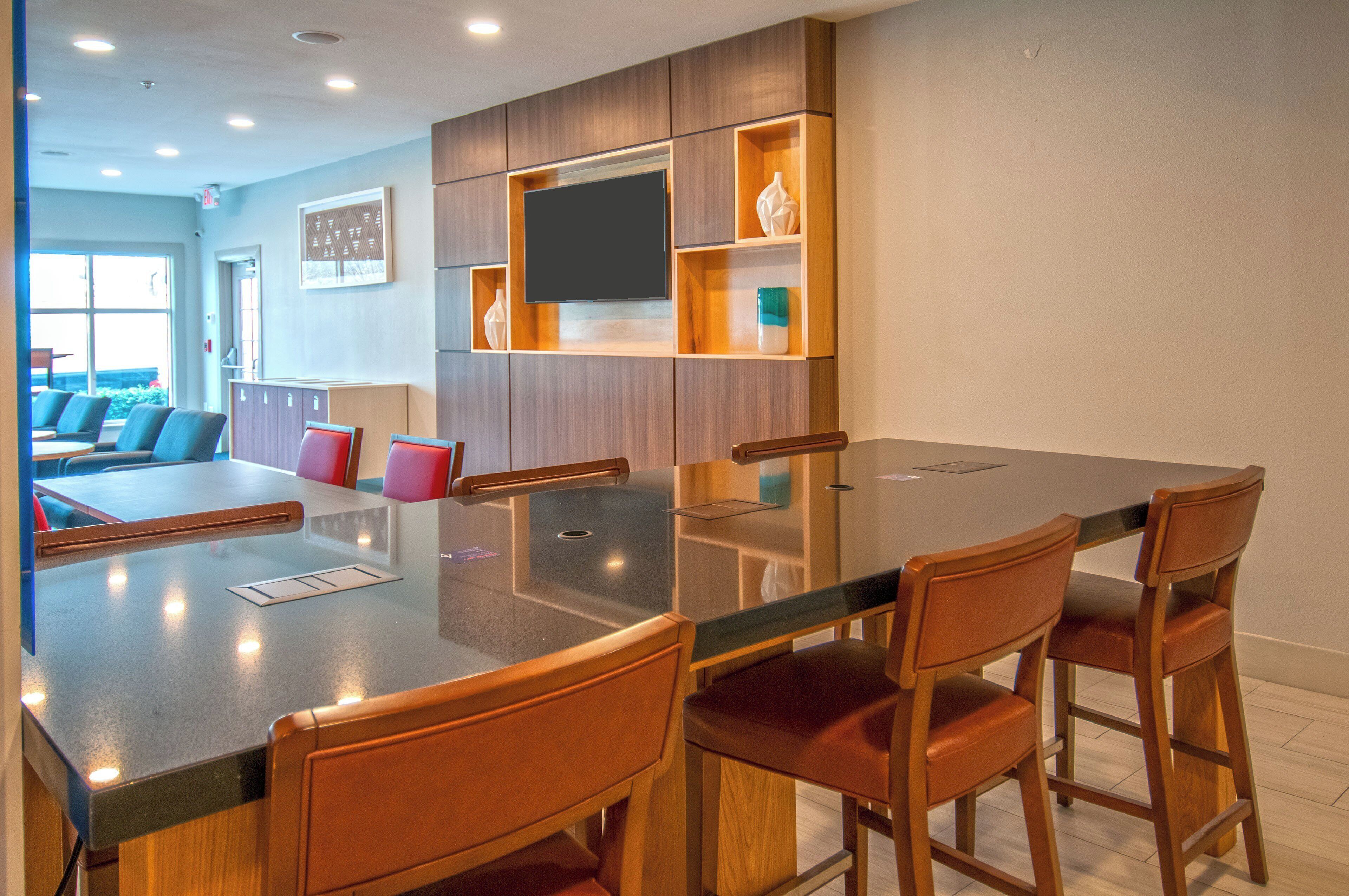 A modern dining area with a glass-top table, wooden chairs, and built-in shelving with decorative items.