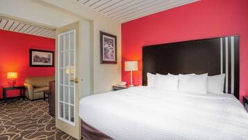 Habitación de hotel con una cama grande, una puerta, una mesita de noche con lámpara, una silla y un cuadro en la pared.