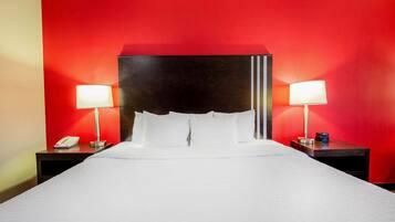 A hotel room with a large bed, two bedside tables with lamps, and a red accent wall.