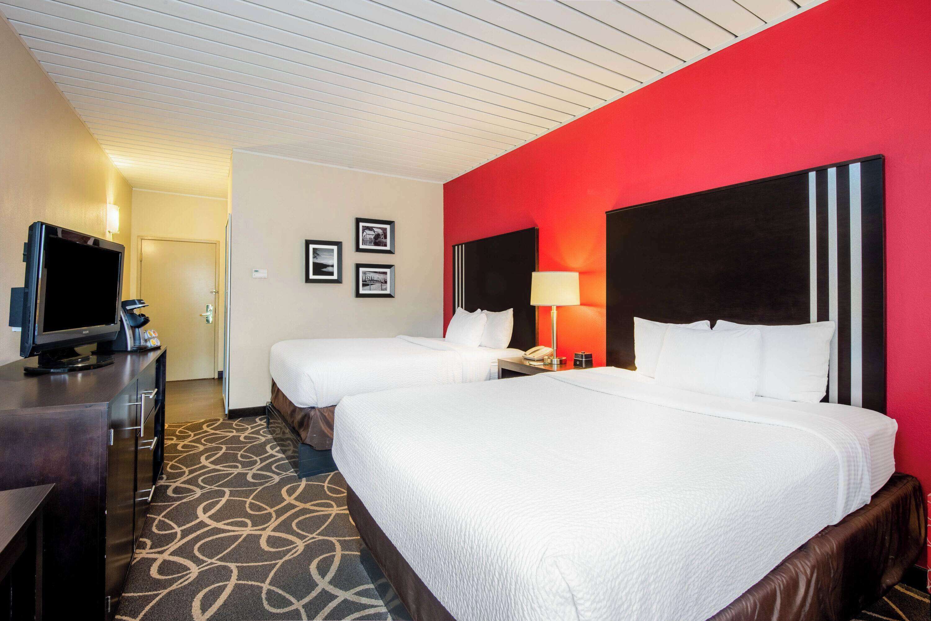 Habitación de hotel con dos camas, televisión, escritorio y una pared de acento roja.