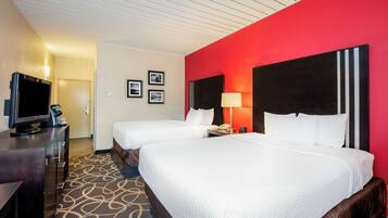 Habitación de hotel con dos camas, televisión, escritorio y una pared de acento roja.