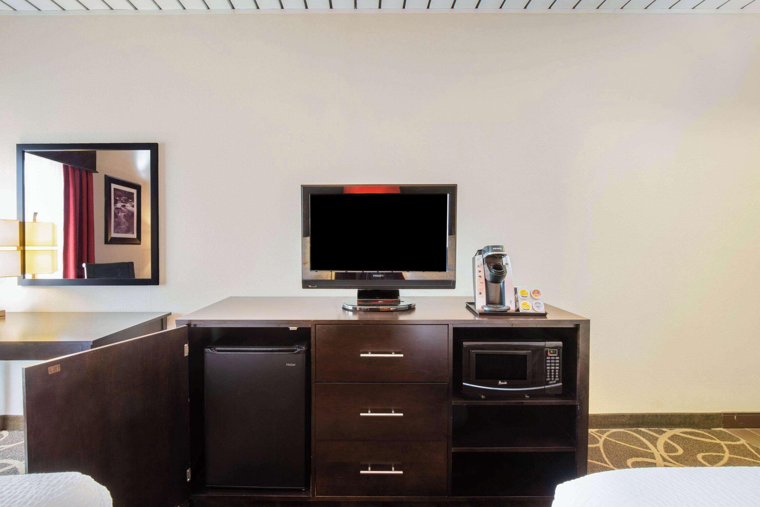 Quarto de hotel com armário de madeira escura, TV de tela plana, micro-ondas e mini geladeira.