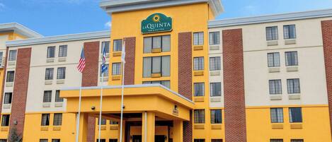 A La Quinta Inn Suites hotel with a yellow facade, multiple windows, and an American flag.