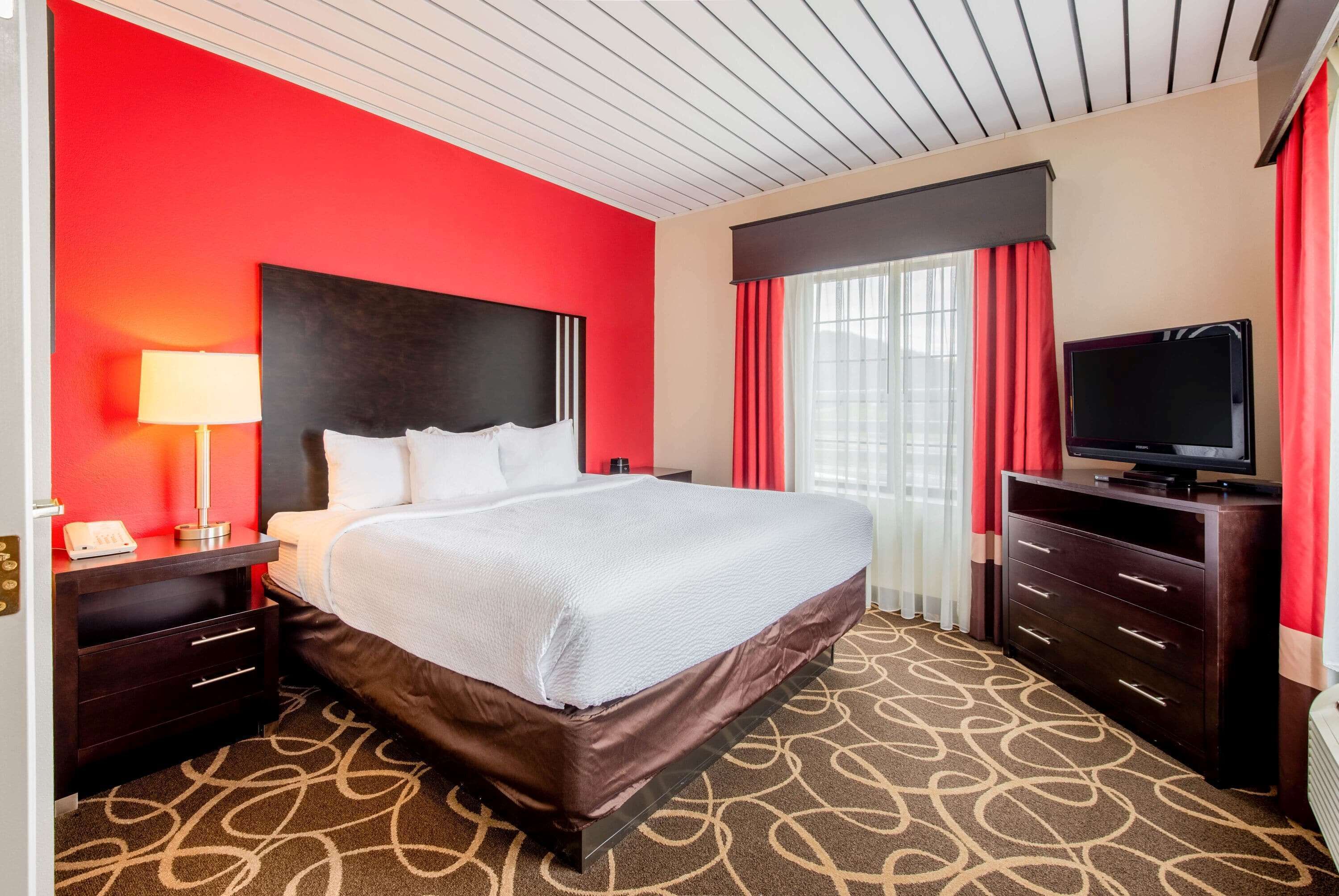 A hotel room with a large bed, a TV, a desk with a lamp, and a window with curtains.