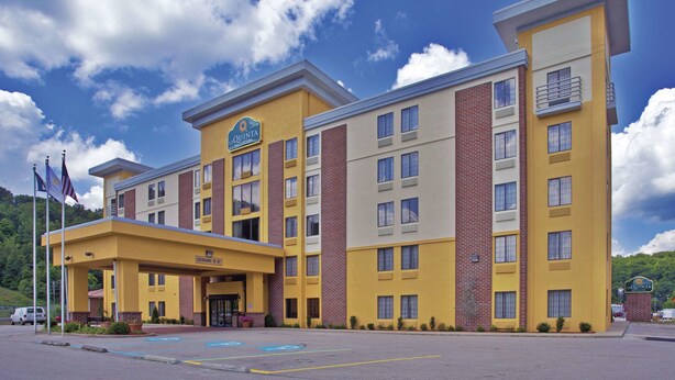 A multi-story hotel with a yellow and brown facade, a covered entrance, and a parking lot. - La Quinta Inn & Suites by Wyndham Elkview - Charleston NE (Elkview)