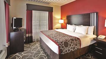 A hotel room with a large bed, a TV on a stand, a desk, and a lamp.