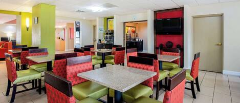 A restaurant with green and red upholstered booths and tables, a kitchen area in the background, and a door to the right.