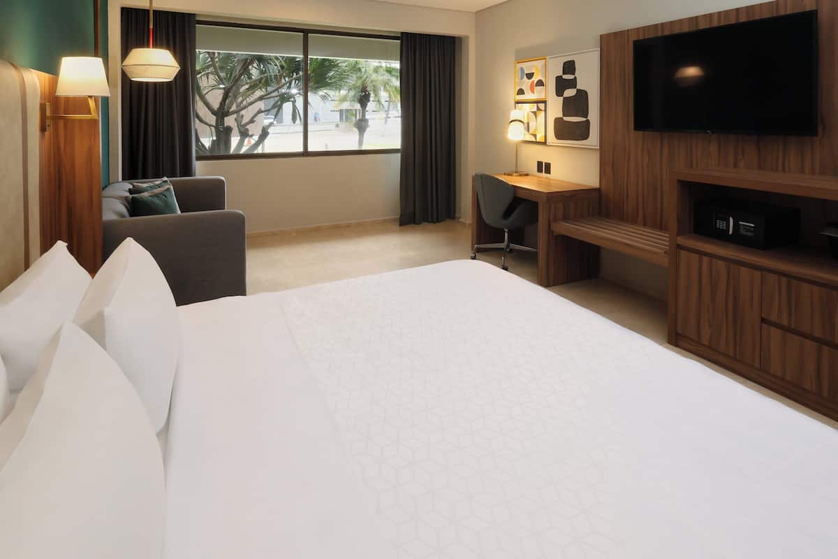 A hotel room with a large bed, a desk with a chair, a TV, and a window with curtains.