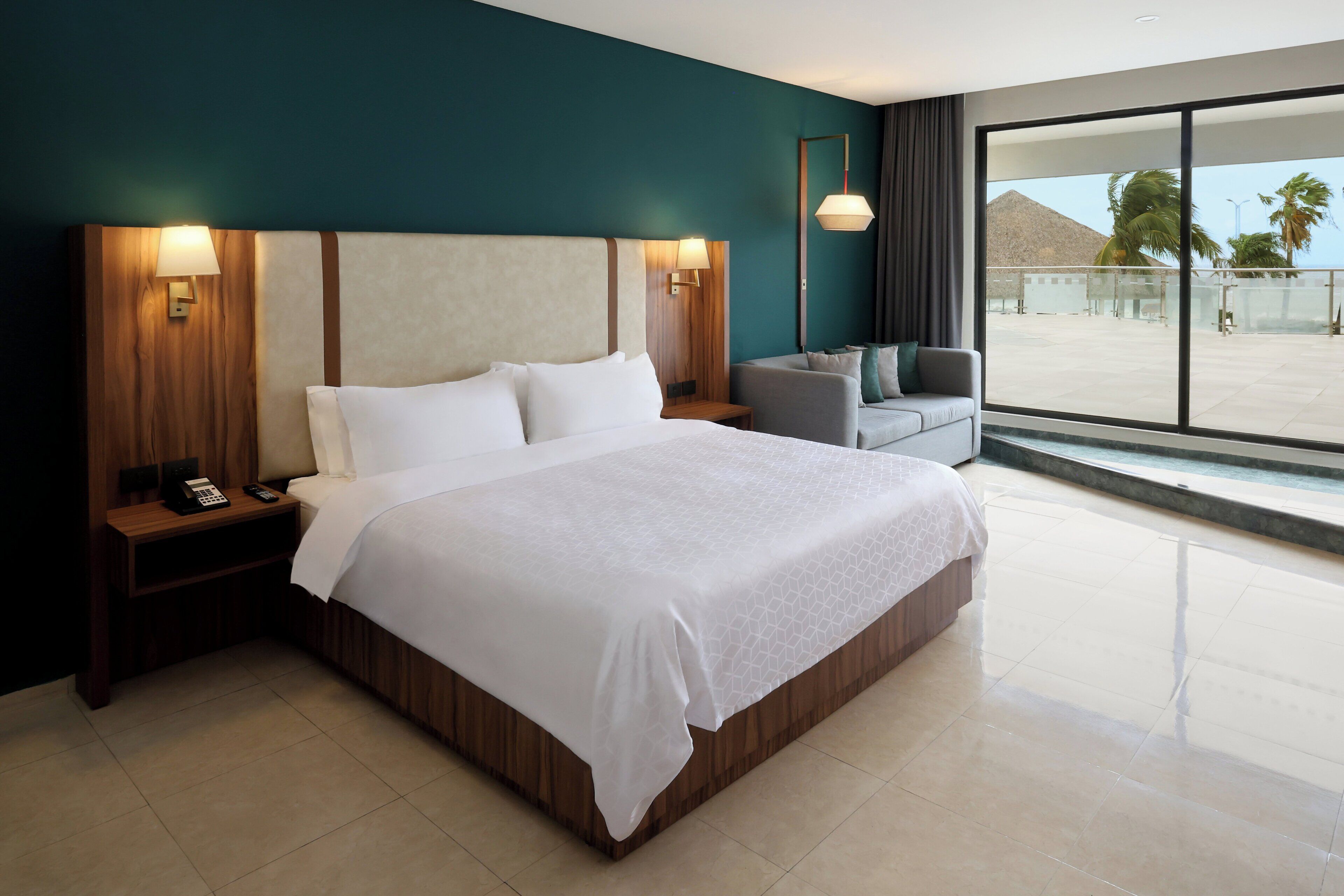 A hotel room with a large bed, bedside lamps, a desk with a phone, a chair, and a view of the outdoors.