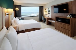 Ein Hotelzimmer mit zwei Betten, einem Schreibtisch, einem Fernseher und Blick aufs Meer.