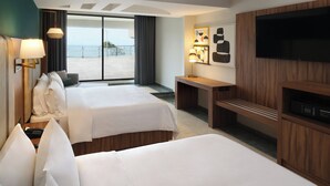Habitació d'hotel amb dos llits, una taula de treball, televisió i una finestra gran amb vista al mar.