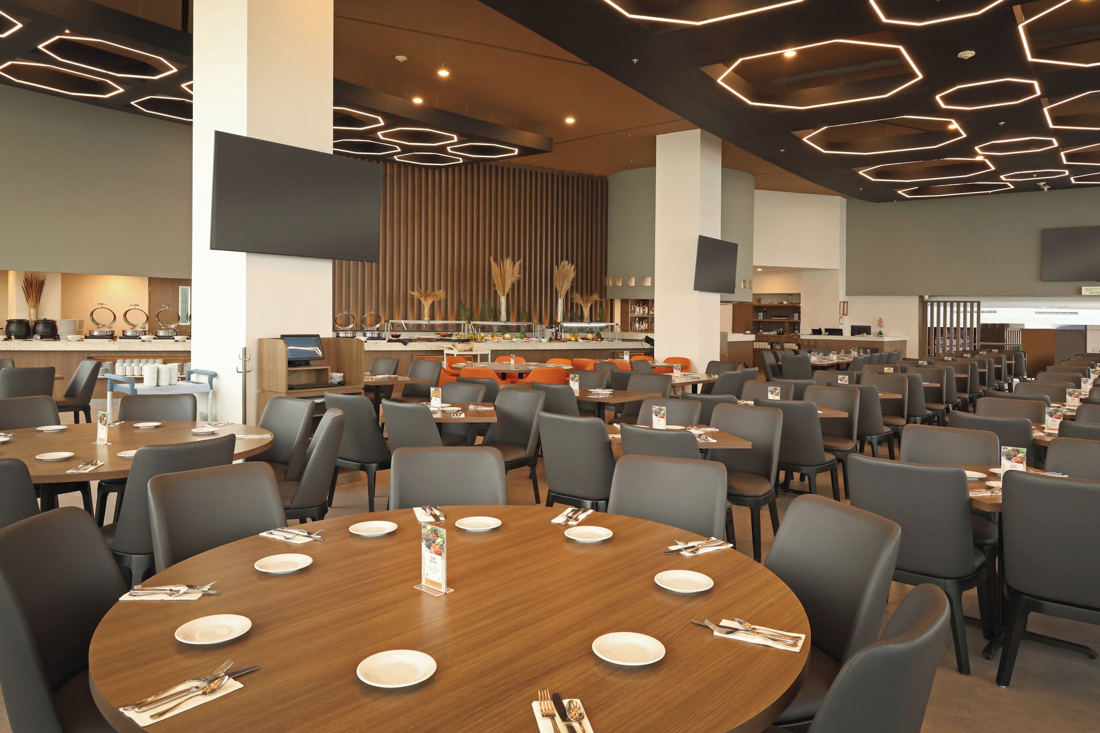 A modern dining area with round tables, grey chairs, and a central buffet.