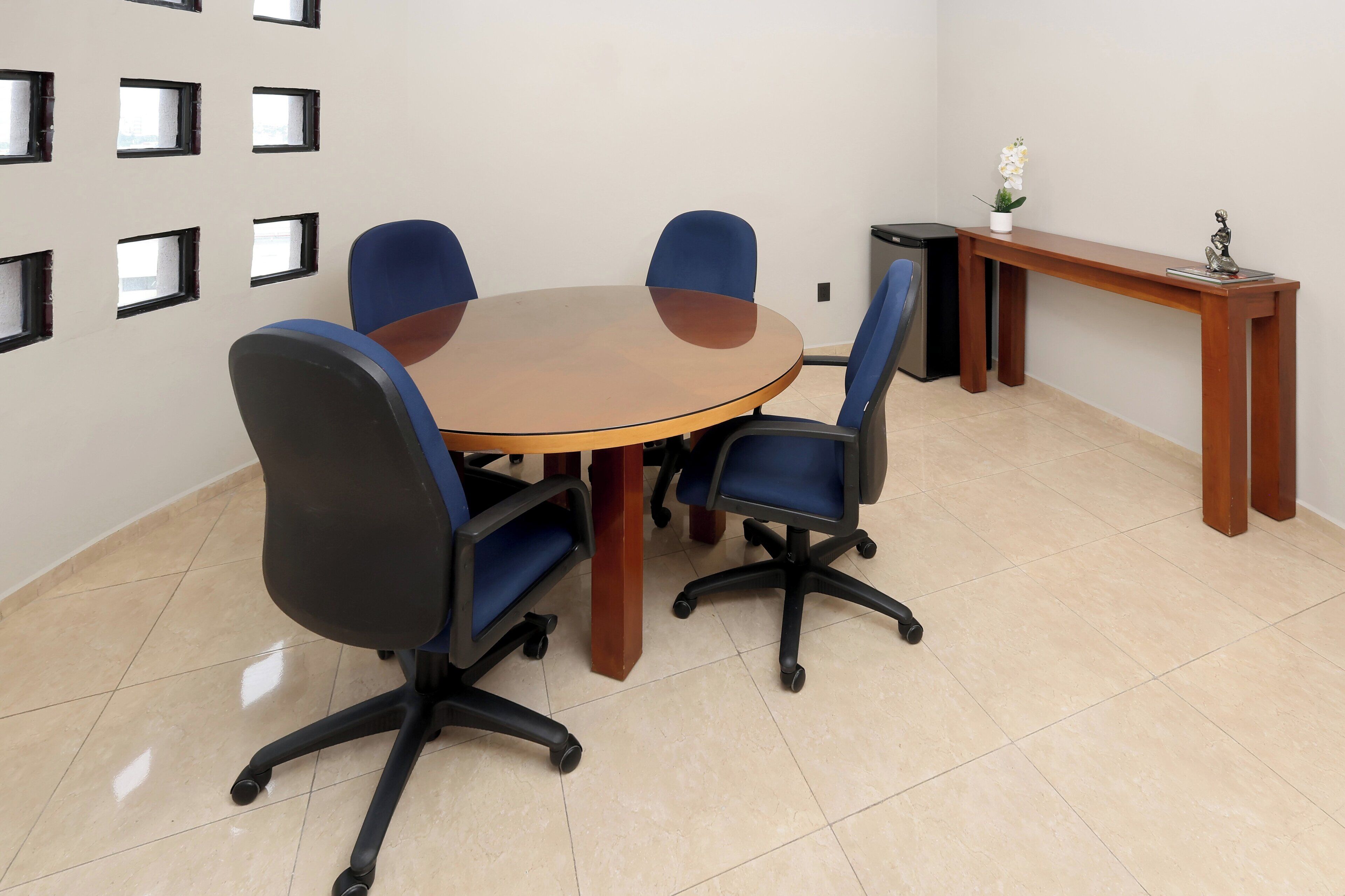 A conference room with a round table, four blue chairs, a wooden bench, and a small potted plant.