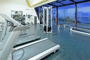 A gym with cardio equipment, weight machines, and a large window with a city view.