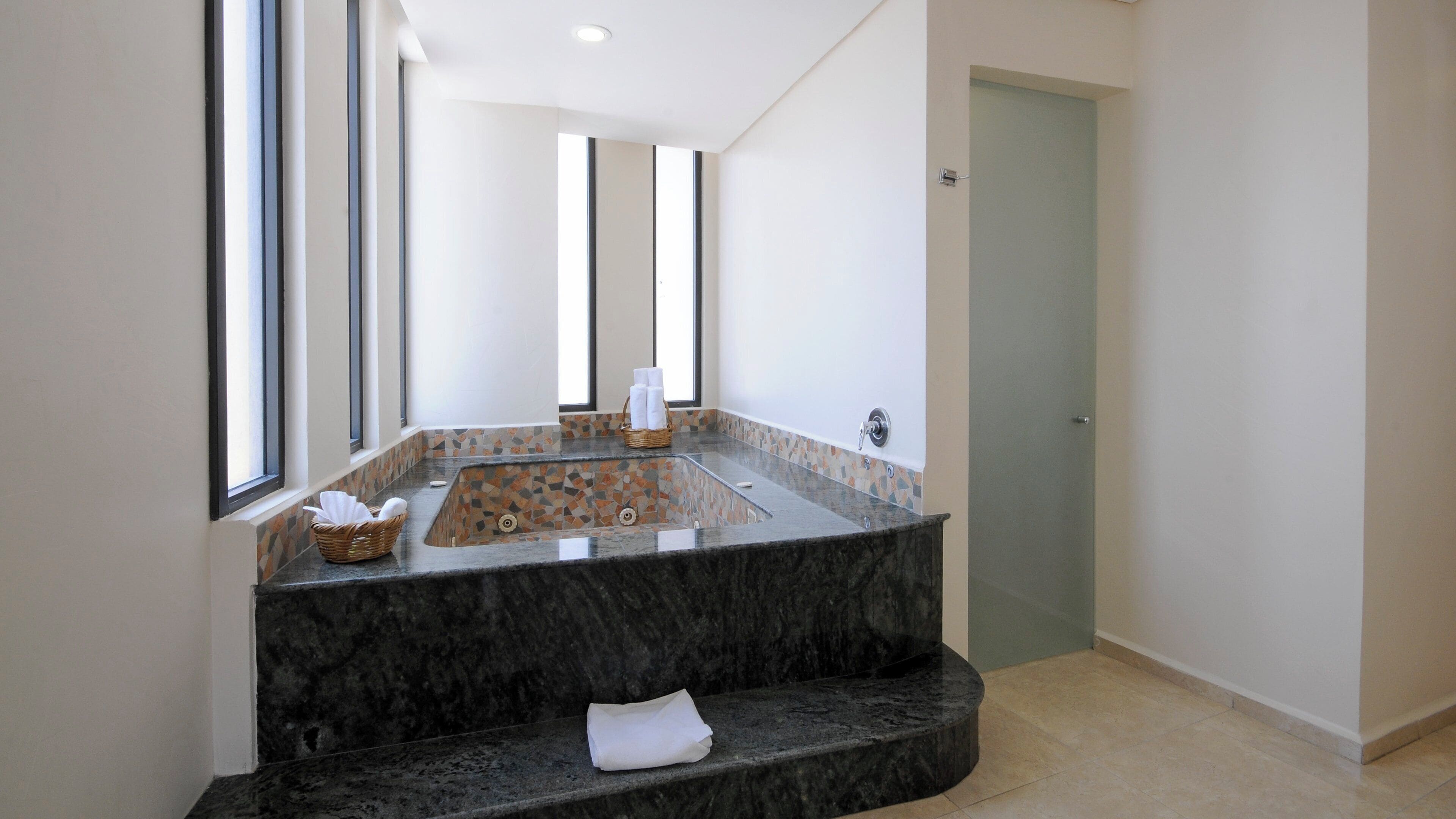 Un baño moderno con lavamanos de mármol, bañera empotrada y un espejo grande.