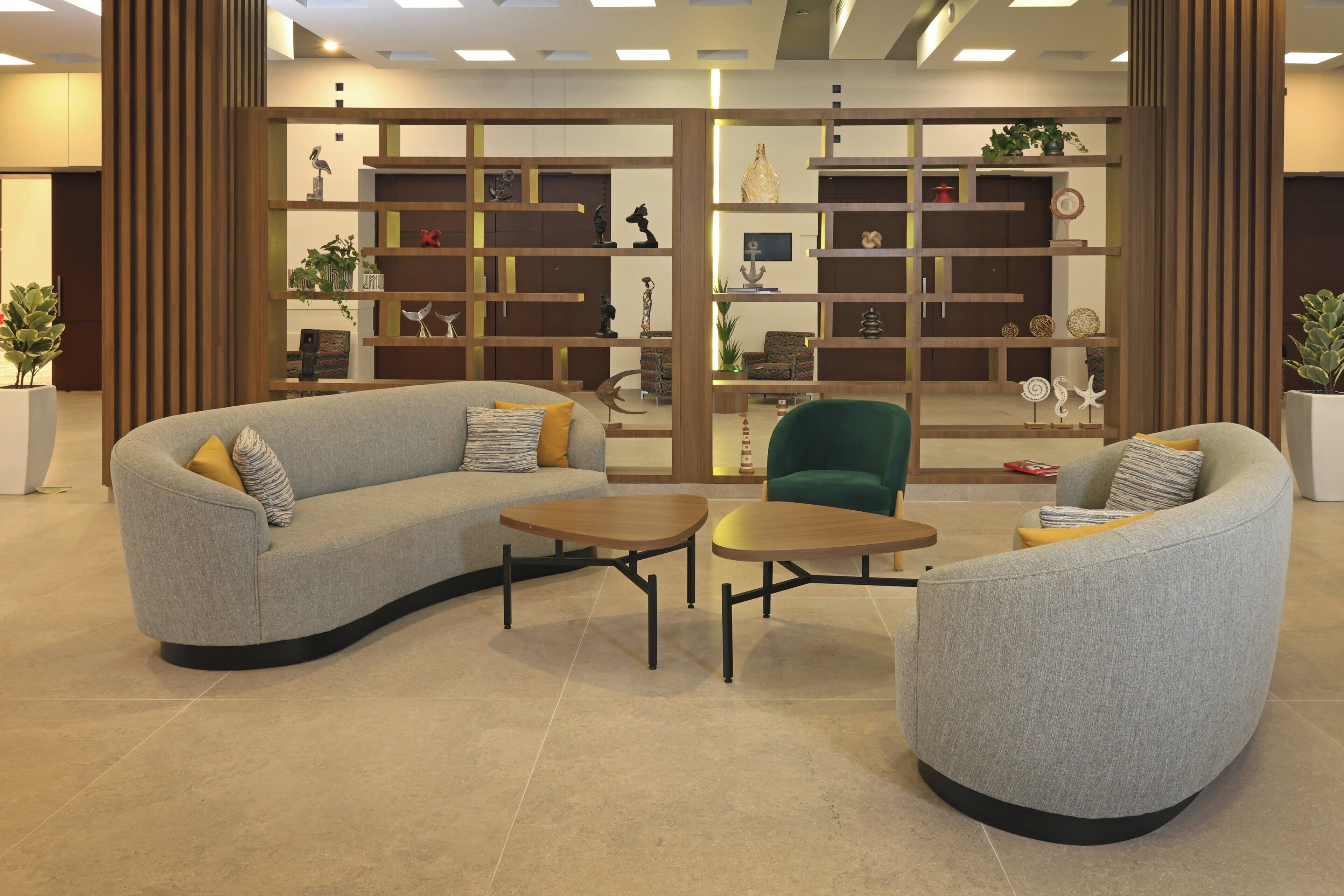 A modern lounge area with a grey sofa, a green armchair, and two small round tables.