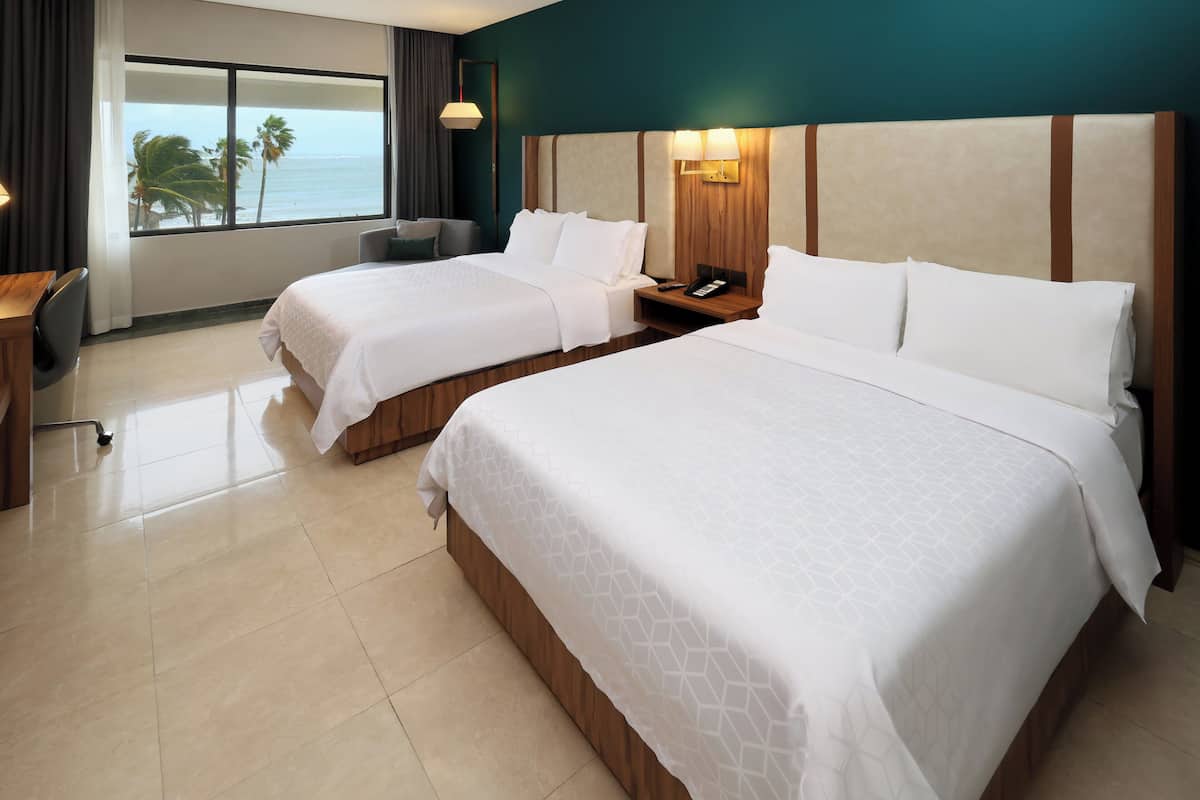 A hotel room with two beds, a desk, and a view of the ocean.