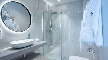Un baño moderno con un espejo redondo, ducha con mampara de vidrio y lavamanos blanco.