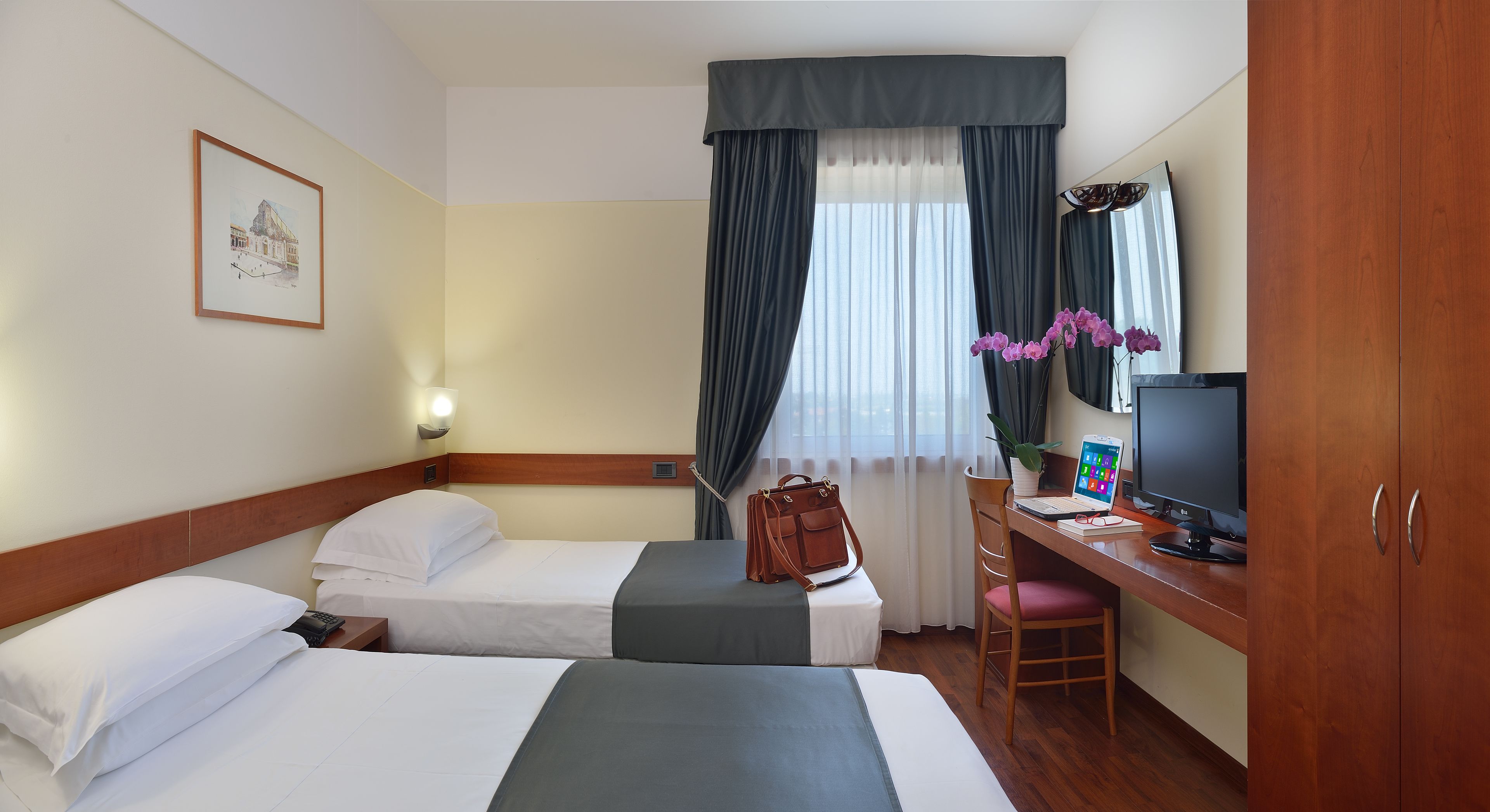 Habitación de hotel con dos camas, un escritorio con computadora, televisión y ventana con cortinas.