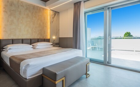 A modern hotel room with a large bed, a bedside table, a nightstand, and a view of the outdoors.