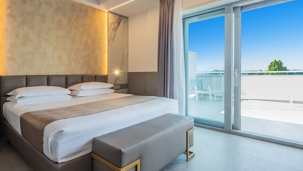 A modern hotel room with a large bed, a bedside table, a nightstand, and a view of the outdoors.