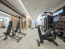 Una palestra moderna con attrezzature cardio, macchinari per pesi e uno schermo televisivo.