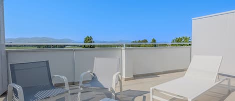 Terraza en la azotea con mobiliario de metal blanco, incluyendo sillas y una mesa, con vistas a un paisaje pintoresco con montañas y vegetación.