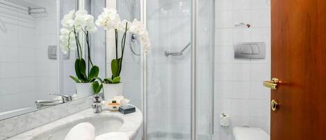 A modern bathroom with a glass-enclosed shower, a marble sink, and a toilet.
