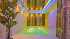 A modern spa room with a large bathtub, a potted plant, and a wall with a marble-like texture.
