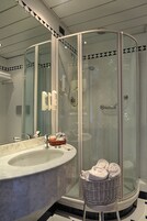Un bagno moderno con doccia vetrata, lavabo in marmo e un cesto in vimini con asciugamani.