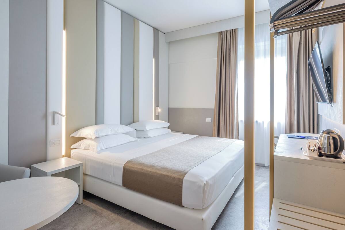 A modern hotel room with a large bed, bedside tables, a desk, and a flat-screen TV.