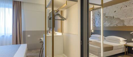 A hotel room with a bed, a desk, a chair, a mirror, and a bathroom with a shower.