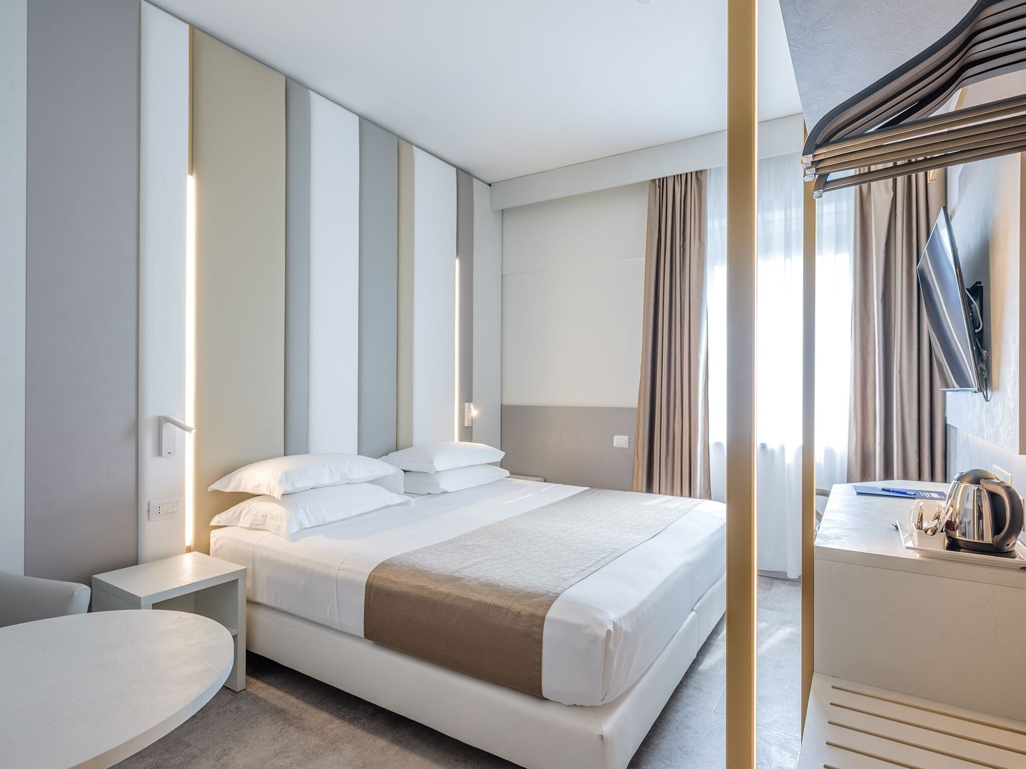 A modern hotel room with a large bed, bedside tables, a desk, and a mirror.
