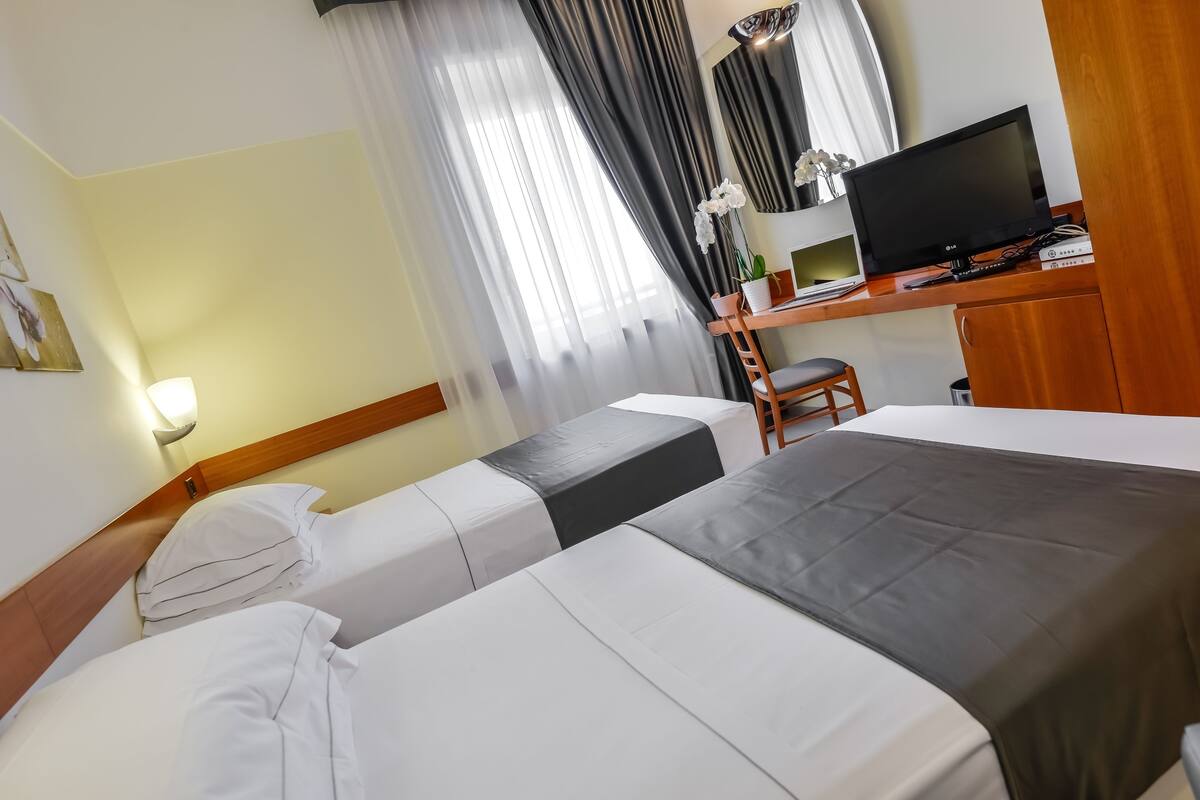 A hotel room with two beds, a desk with a TV, and a chair.