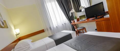 A hotel room with two beds, a desk with a TV, and a chair.