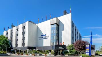 A modern hotel with a prominent sign, multiple flags, and a clear sky.