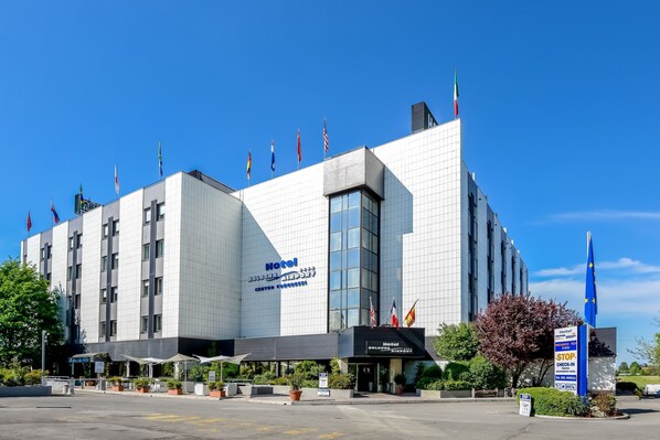 A modern hotel with a prominent sign, multiple flags, and a clear sky.